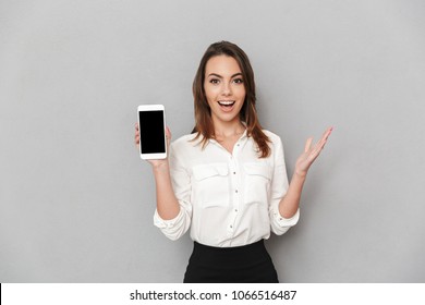 Portrait Of An Excited Young Business Woman Showing Blank Screen Mobile Phone Isolated Over White Background