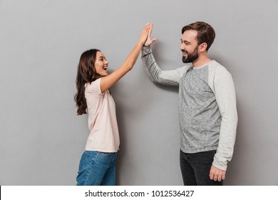 Portrait Of An Excited Young Couple Giving High Five Over Gray Background