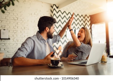 Portrait of an excited young couple giving high five while shopping online.