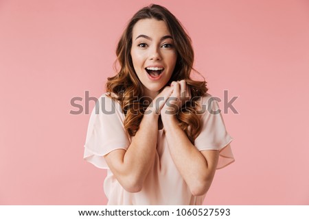 Portrait of an excited young girl in dress looking at camera isolated over pink background