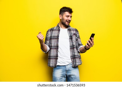 Portrait Of An Excited Young Man Looking At Mobile Phone Isolated Over Yellow Background