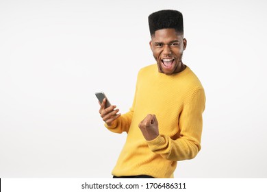 Portrait Of Excited Young Man With Mobile Phone Isolated Over White Background And Celebrating