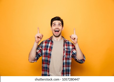 Portrait of an excited young man pointing fingers up at copy space isolated over yellow background