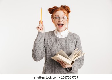 Portrait Of An Excited Young School Nerd Girl Holding Book And Pointing Up Isolated Over White Background