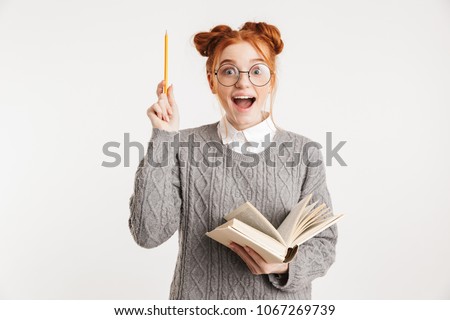 Portrait of an excited young school nerd girl holding book and pointing up isolated over white background