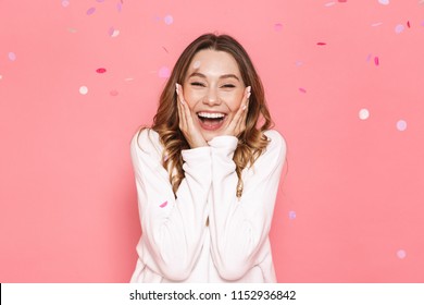 Portrait Of An Excited Young Woman Celebrating Under Confetti Shower Isolated Over Pink Background