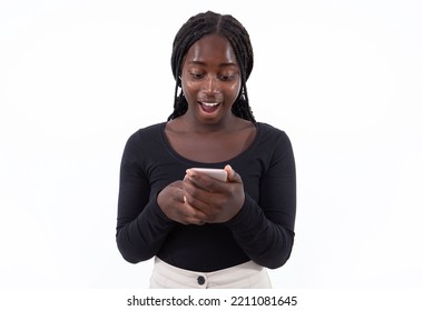 Portrait Of Excited Young Woman Reading News On Smartphone. Braided African American Lady Wearing Black Longsleeve Surfing Internet On Mobile Phone. Good News And Success Concept