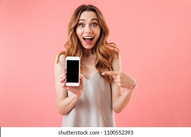 Portrait Of An Excited Young Woman Showing Blank Screen Mobile Phone Isolated Over Pink Background