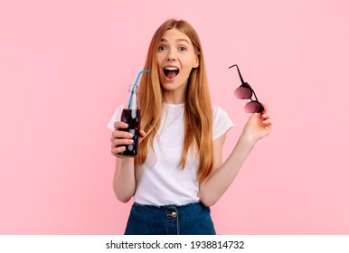 Portrait Of Excited Young Woman In Sunglasses Holding Carbonated Drink On Pink Background