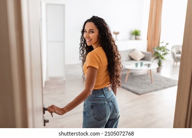 Portrait Of Excited Young Woman Walking In Her Apartment, Entering New Home And Looking Back At Camera, Happy Curly Lady Standing In Doorway Of Modern Flat, Coming Inside, Selective Focus