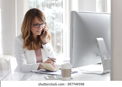 Portrait Of And Executive Middle Aged Businesswoman Sitting In Front Of Computer And Making Call While Working In Her Office.