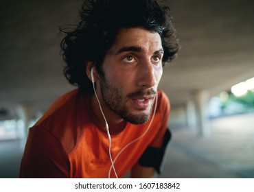 Portrait of a exhausted sweaty serious young male runner with earphone in his ears relaxing after running looking into the distance