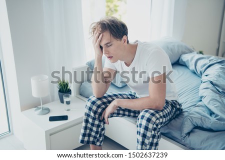 Portrait of exhausted unhappy man after hangover party have terrible fatigue migraine catch cold suffer sit on bed wear checkered plaid pajama in house indoors