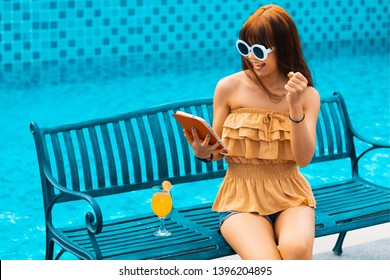 Portrait of an Exited young asians girl looking her mobile phone,smart phone or tablet sit on chair beside swimming pool. - Powered by Shutterstock