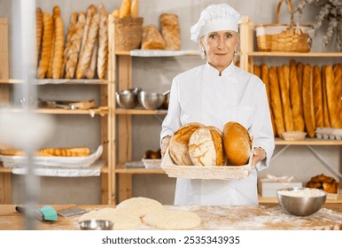 Portrait of experienced female baker holding fresh rustic bread in her hands - Powered by Shutterstock