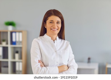 Portrait Of An Experienced Friendly Middle-aged Doctor Woman Standing In Hospital With Folded Arms And Looking At Camera. Concept Of Healthcare, Experienced Clinic Staff And Professional Medical Care.