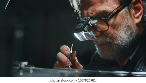 Portrait of experienced goldsmith working on a handmade jewelry ring with precious diamond stones in a workshop. Concept of jewelry, luxury, goldsmith, diamonds, brilliance.