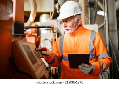 Portrait of an experienced industrial engineer or senior factory worker operating automated machine in production hall. Factory interior in background. - Shutterstock ID 2120861291
