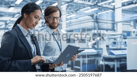 Portrait of Experienced Male and Female Engineers Standing in Agency Room, Using Computer Devices and Discussing Production at a Modern Automated Electronics Manufacture with Robot Arms