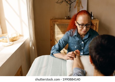 Portrait Of Experienced Middle Aged Female Acupuncturist With Red Hair Sitting At Massage Table Feeling Pulse Of Female Patient. Traditional Eastern Chinese Medicine And Health Care Concept