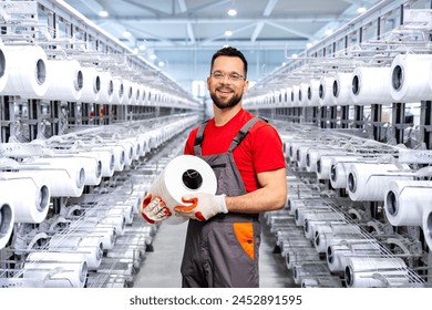 Portrait of experienced worker in textile factory holding thread spool and standing by industrial knitting machine. - Powered by Shutterstock