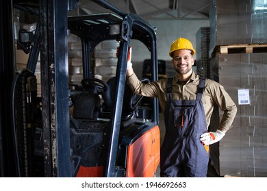 Portrait of experienced young caucasian forklift driver standing by loading cargo machine in storage warehouse.