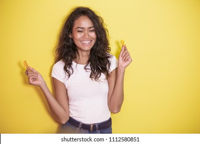 portrait of expressive asian woman eating potato chips on yellow background