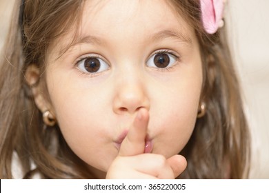 Portrait of expressive beautiful little girl finger up to lips for making a quiet gesture. Girl showing silence gesture looking at the camera