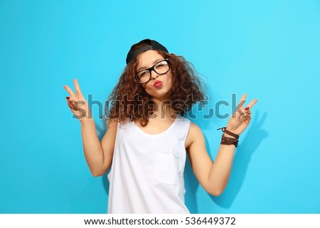 Portrait of expressive young model with cap and glasses on blue background