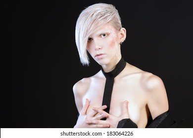 Portrait of an extravagant naked model with boyish make-up and haircut. Black background. 