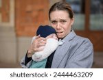 Portrait of a extreme exhaused and stressed late-term mother in her 40s holding her newborn baby and crying to the camera outdoor
