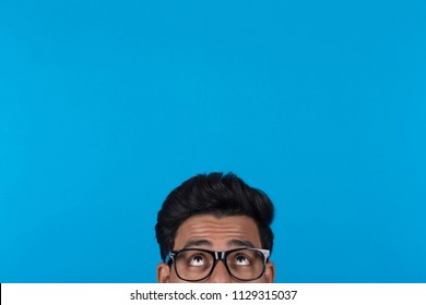 Portrait Of Eyes Looking Up Wearing Glasses Hiding Behind Something On A Blue Background.