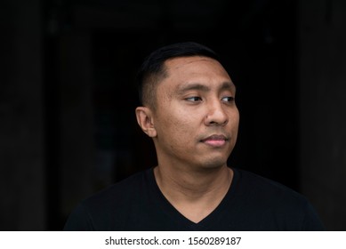 Portrait Of The Face Of An Asian Indonesian Man Looking Pensive, Serious And Thoughtful, He Turns His Face Away To The Side Not Looking At The Camera, With Black Background