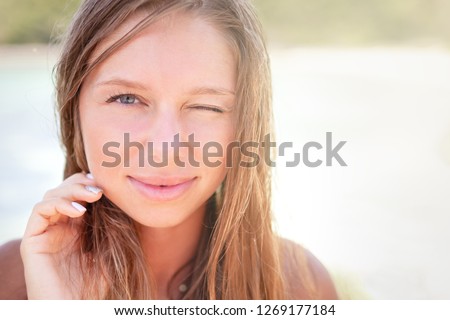 
portrait face of a beautiful young girl sunbathing in the sun on the beach paradise looks with one eye wink and squinting at a very bright sunny warm day and smiling