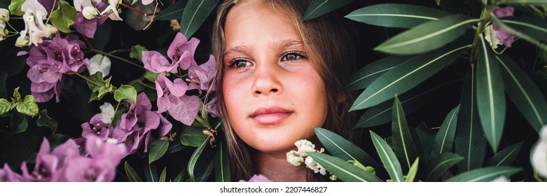 portrait face of candid beautiful little kid girl of eight years old with brown eyes on background of green plants and pink flowers during a summer vacation travel. gen z mental health concept. banner - Shutterstock ID 2207446827