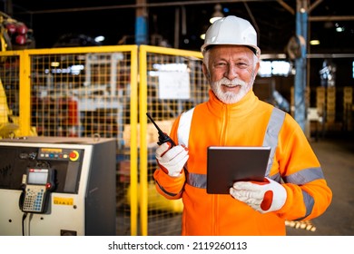 Portrait Of Factory Worker Holding Radio Communication And Standing In Front Of Industrial Production Machine.