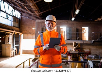 Portrait of factory worker in orange high visibility vest and hard hat controlling process of production via tablet computer. In background industrial machines and interior. - Powered by Shutterstock