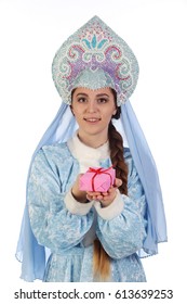 Portrait of a fairy-tale Snow Maiden in a blue suit and kokoshnik with a veil, gives a gift in a pink box