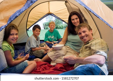 Portrait Of Family Camping Sitting Inside Tent In Garden Eating Breakfast