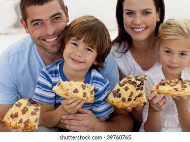 Portrait Of Family Eating Pizza On Sofa At Home