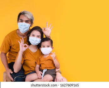 Portrait Of Family Group Showing Ok Sign And Wearing Protective Mask Trying To Protect From Virus Epidemic Over Yellow Background.