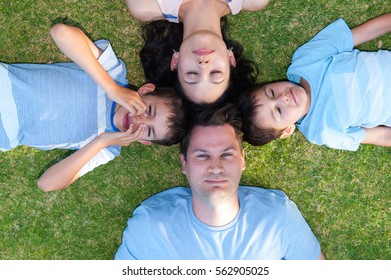 Portrait family lying head to head in circle on grass, happy relaxed bonding, children and their parents.