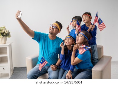 Portrait Of Family With Malaysian Flag Take Selfie Together Using Smartphone