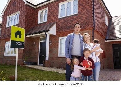 Portrait Of Family Outside New Home With Sold Sign