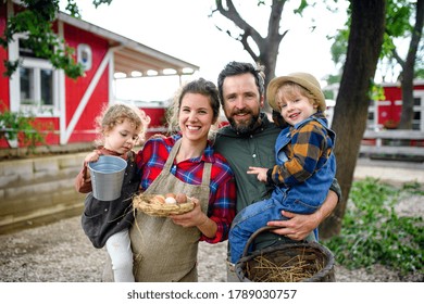 Portrait Of Family With Small Children Standing On Farm, Holding Basket With Eggs.