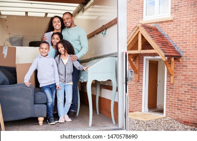 Portrait Of Family Standing On Tailgate Of Removal Truck Outside New Home