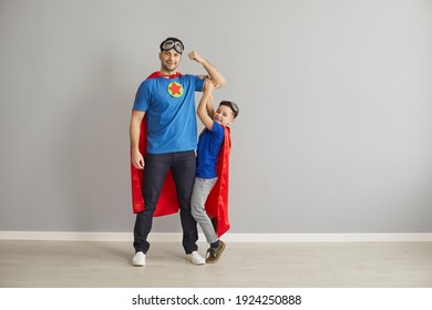 Portrait of family with super powers. Happy young dad and little child dressed as superheroes playing and having fun together. Father and son in hero capes standing in studio and looking at camera