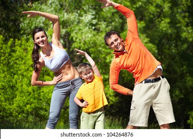 Portrait Of Family Of Three Doing Physical Exercise In Park