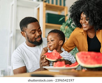 Portrait of family of three, father, mother and son cutting a watermelon fruit and having fun in the kitchen at home, healthy food and family bonding concepts - Powered by Shutterstock