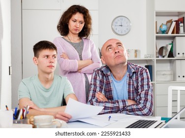 Portrait of family of three with teenage son worried about debts on bills working with papers at home - Shutterstock ID 2255921433